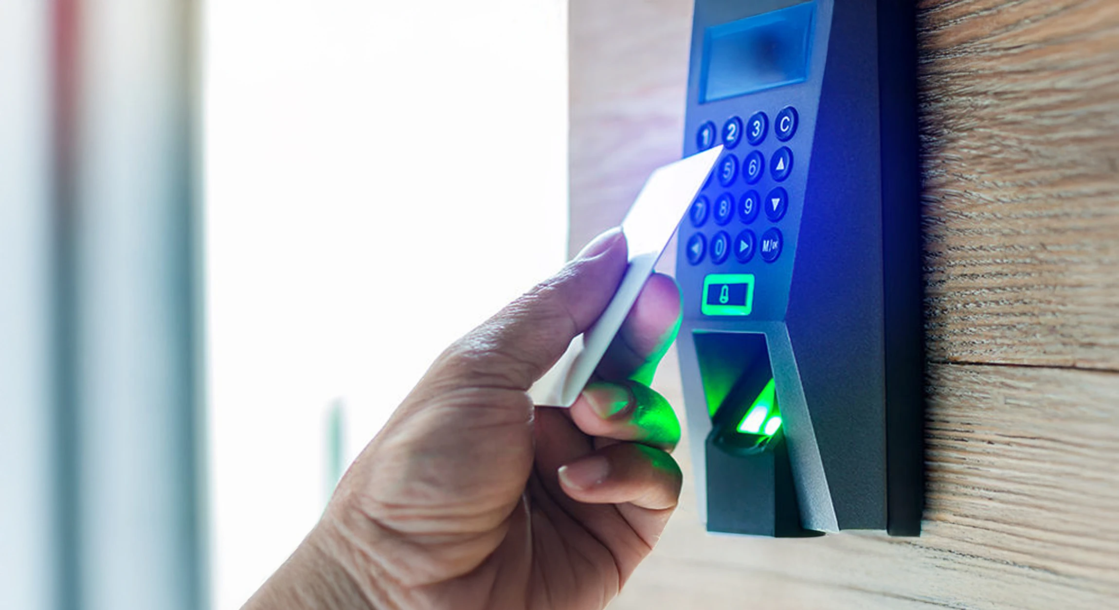 Une main tenant une carte blanche vierge au-dessus d'un lecteur de carte d'accès noir avec voyants LED sur fond bleu