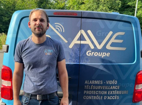 Agent de sécurité en uniforme bleu avec casquette "SECURITY" et masque chirurgical, assis à un bureau de surveillance